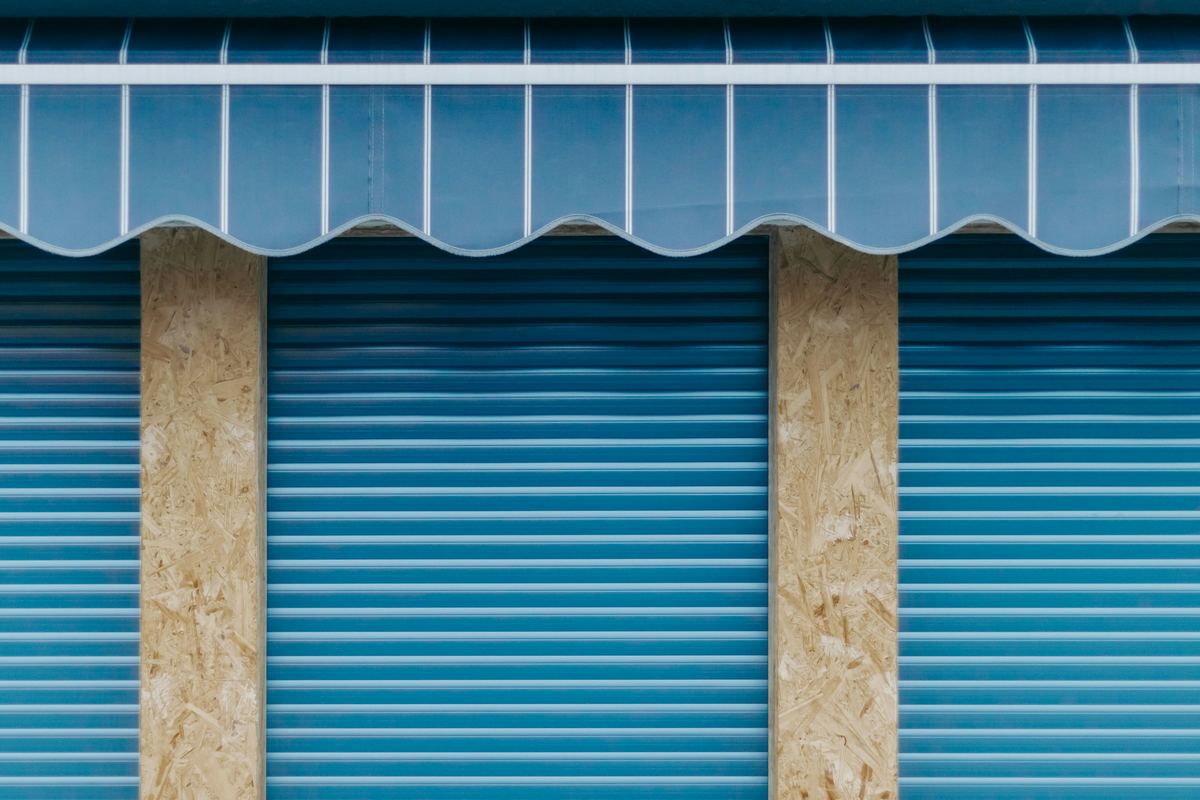 Blauw zonnescherm boven drie gesloten rolluiken