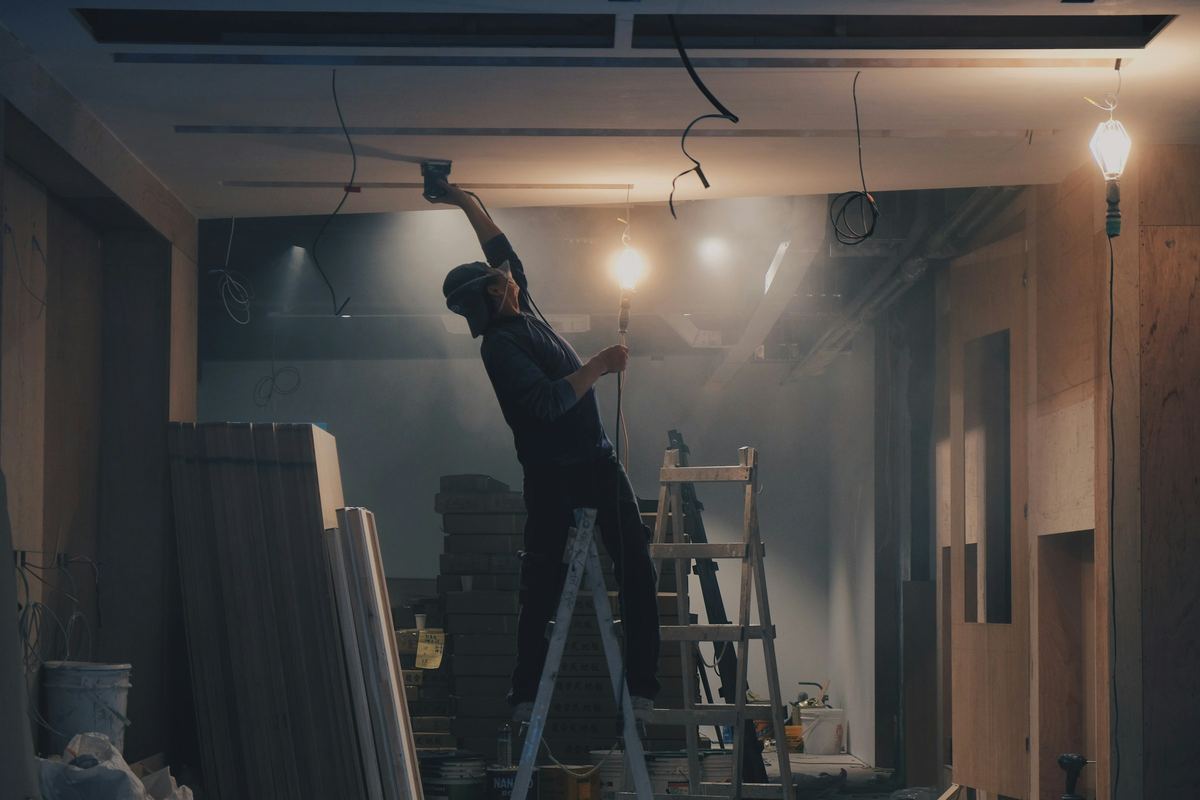 Vakman op een ladder legt bekabeling voor plafondlampen in een ruimte in verbouwing