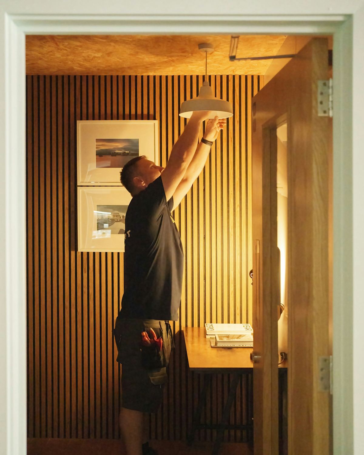 Vakman hangt een witte hanglamp op in een kamer met houten latten